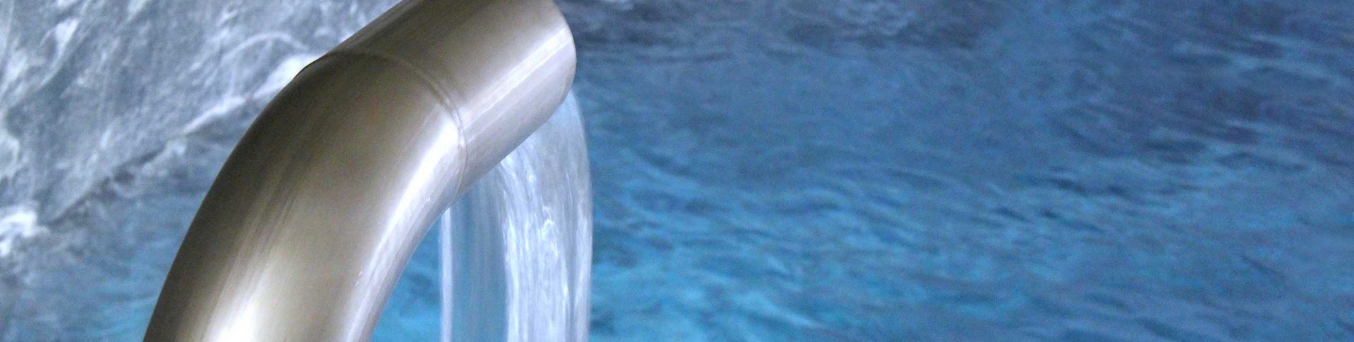 Wasser fließt aus einem silbernen Rohr in ein Wasserbecken.