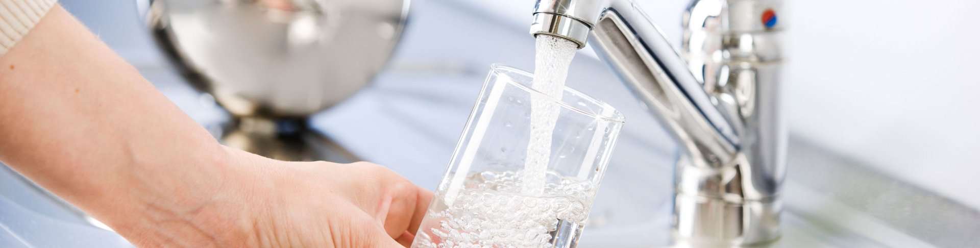 Person lässt sich Leitungswasser aus dem Wasserhahn in ein Glas ein.
