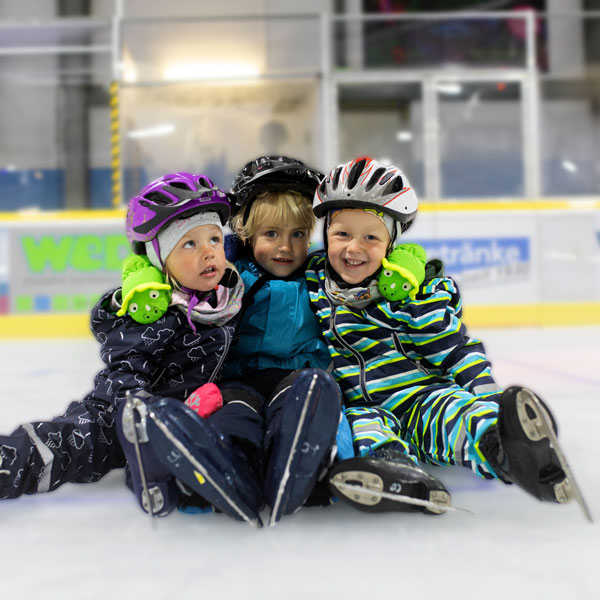 Kinder sitzen lachend auf der Eisfläche der Eishalle.