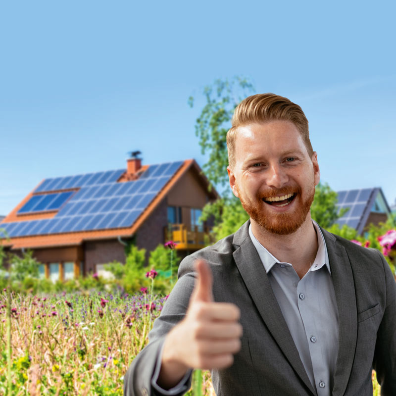 Mann steht lachend und mit Daumen nach oben vor Häusern mit Photovoltaikanlagen.