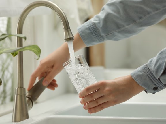 Eine Person gießt sich Wasser aus dem Wasserhahn in eine Glas ein